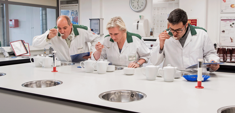 Three people tasting coffee in a white coat in a lab.